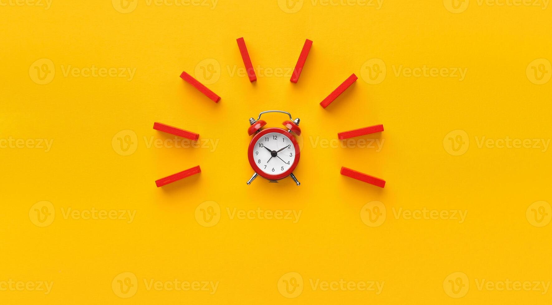 Alarm clock with red wooden dominoes on yellow background. Minimalism concept, panorama with empty space photo