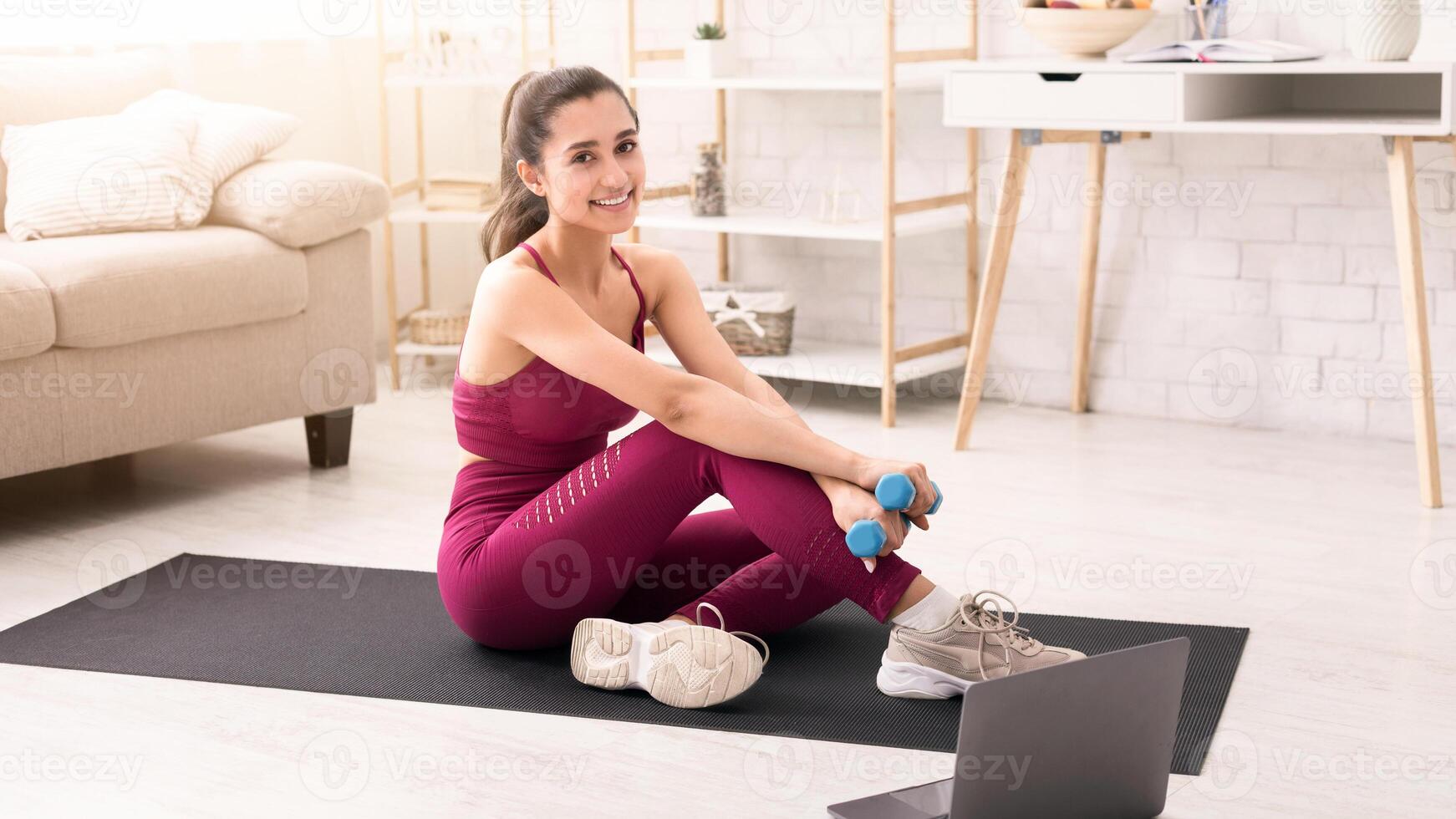 Home training. Smiling Latin woman with dumbbells watching workout tutorial in light room photo