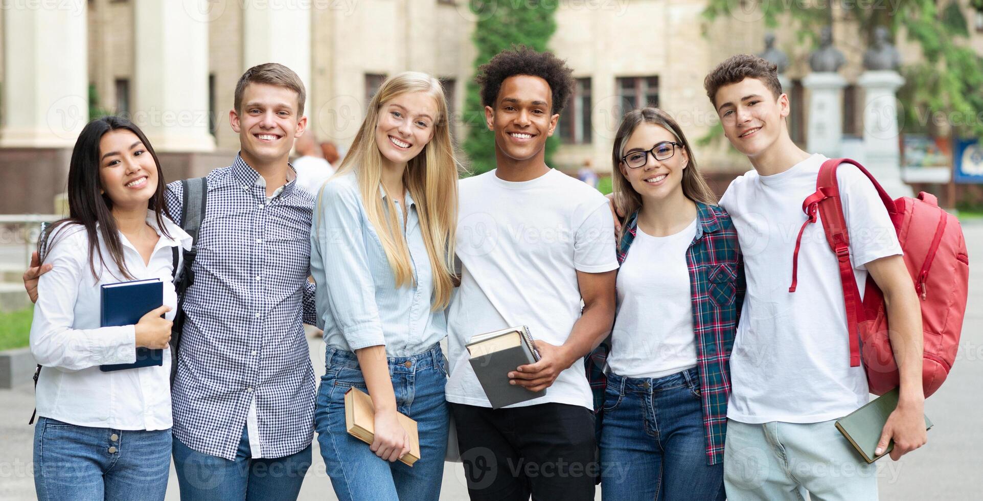 Diverse students in campus, posing in front of university and looking at camera photo
