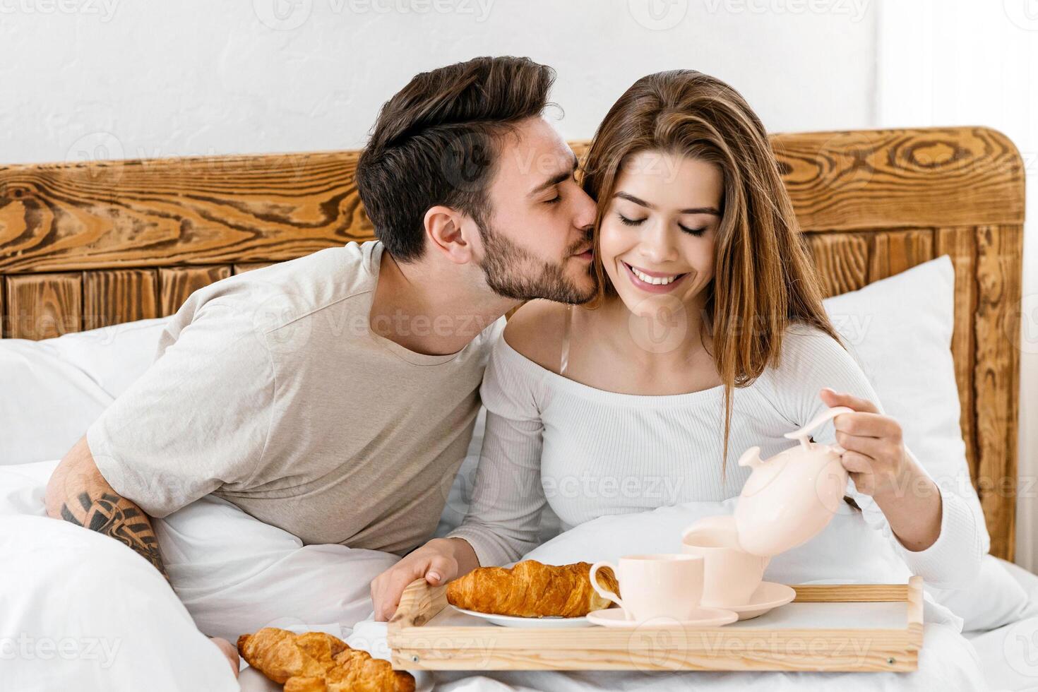 Breakfast in bed. Husband kisses wife on cheek, happy wife pours coffee photo