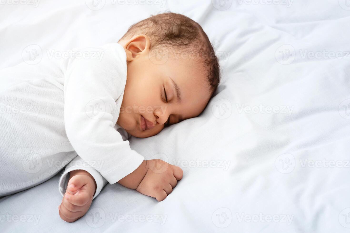 Beautiful Little Baby Boy Sleeping Peacefully Lying On Side In Bed Indoors, Resting During Daytime Sleep With Eyes Closed. Toddler Child Napping Indoors. High Angle, Cropped Shot With Copy Space photo