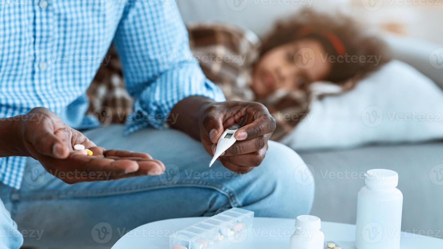 Contagious disease outburst. African American male holding pills and thermometer, sick child on background. Copy space photo