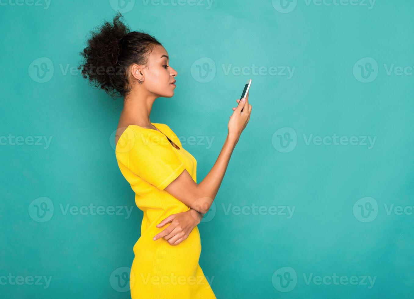 Young african-american woman typing message on smartphone on blue studio background, side view. Communication concept photo
