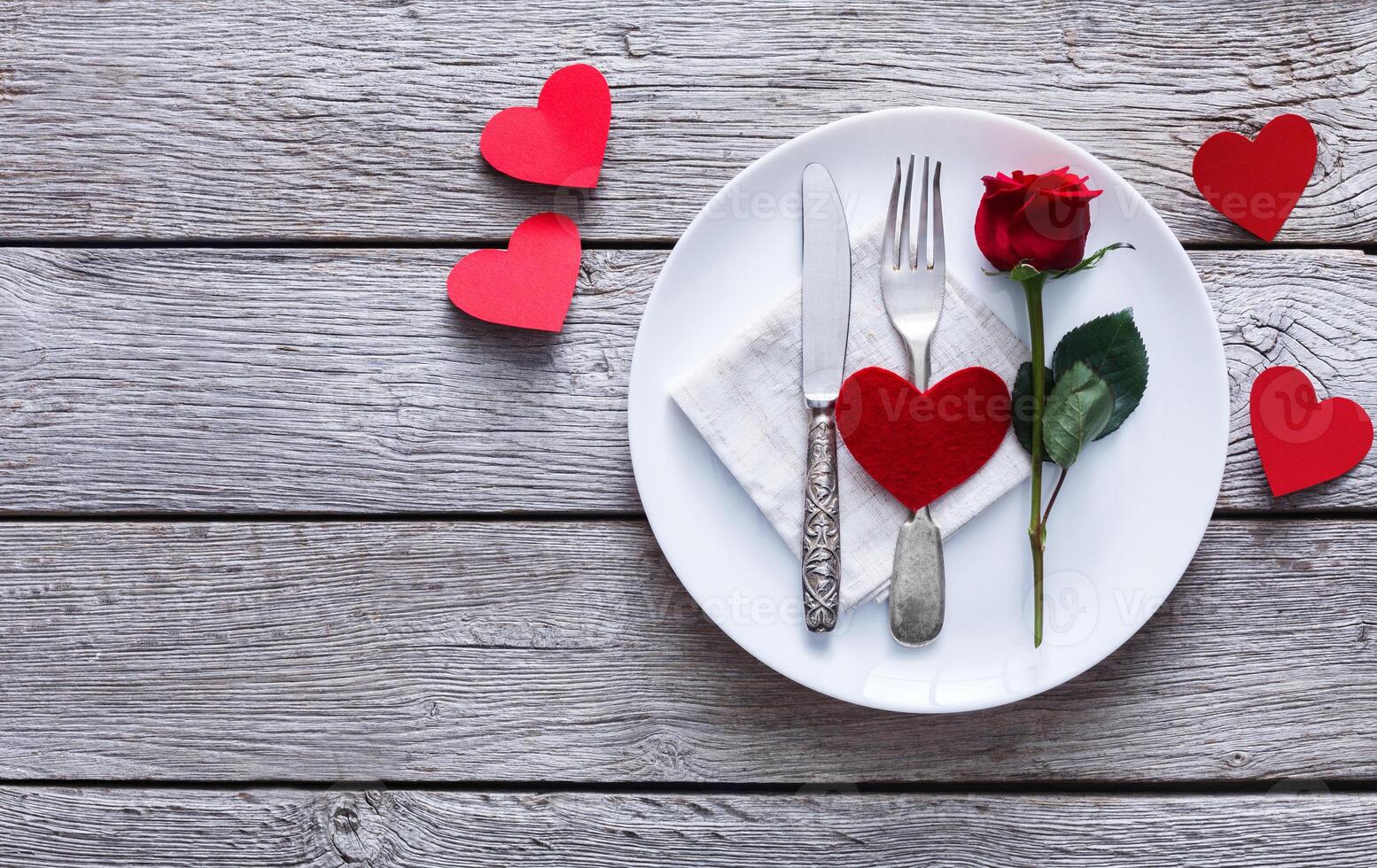 Romantic dinner concept. Valentine day or proposal background. Top view of restaurant wooden table with heart and rose with cutlery on plate. Copy space on rustic wood photo