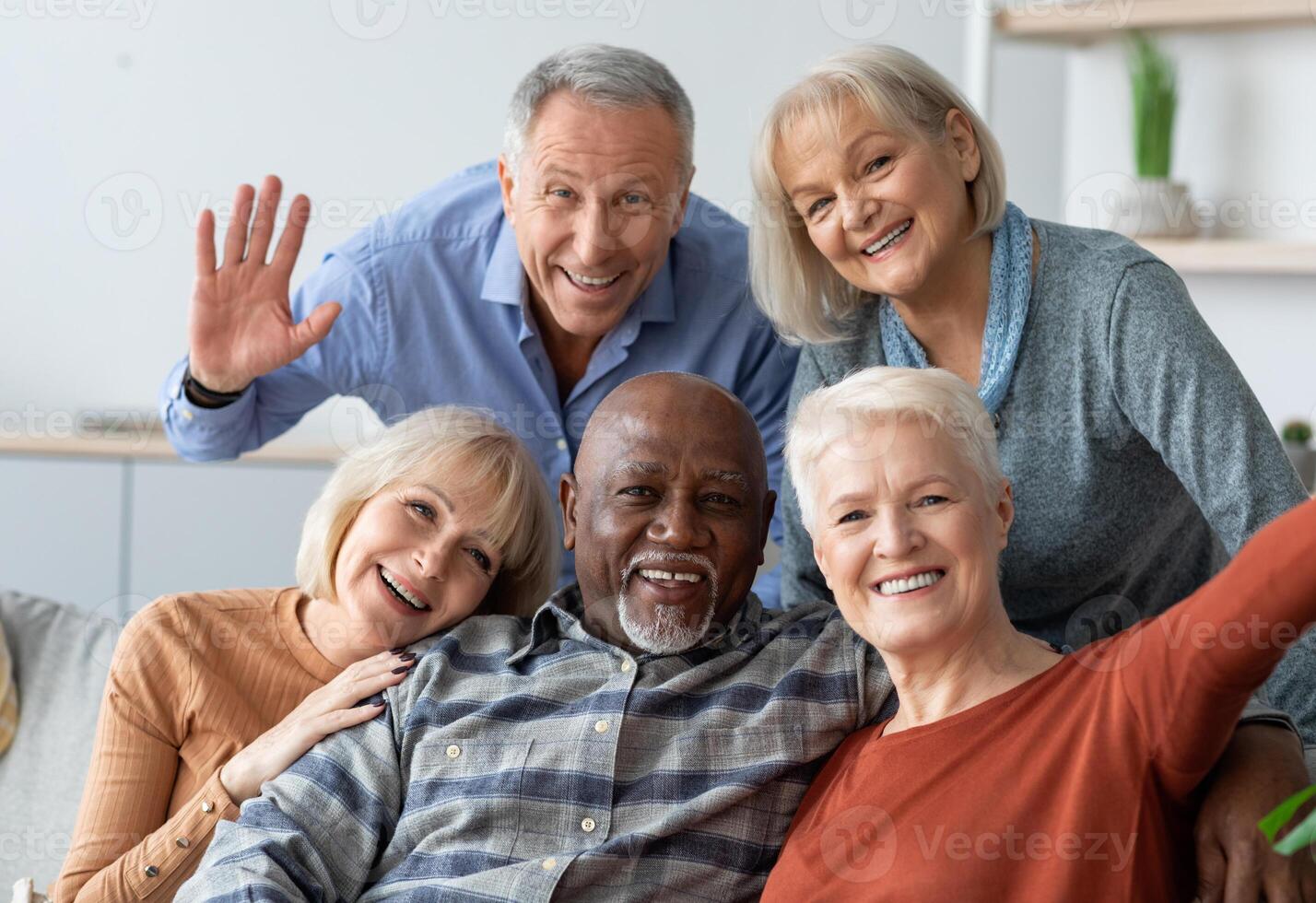 Multiracial group of happy positive elderly people men and women in casual outfits taking selfie together while chilling together, hugging and smiling at camera, nursing home interior photo