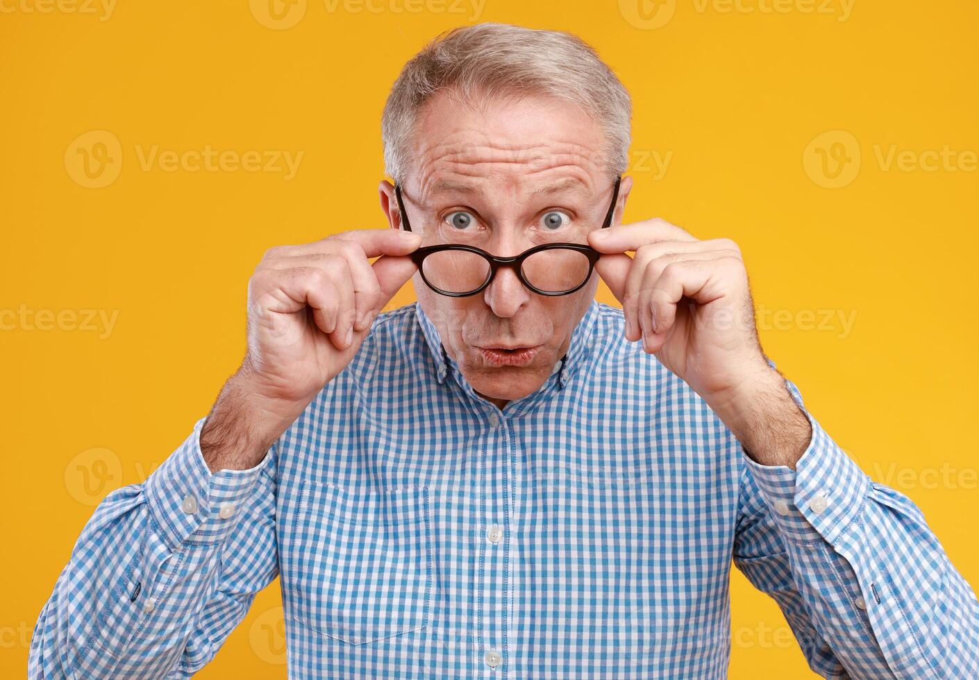 Wow, Omg. Closeup portrait of surprised amazed mature man looking staring at camera taking off eyeglasses, shocked by news or special offer, standing isolated on yellow orange studio background photo