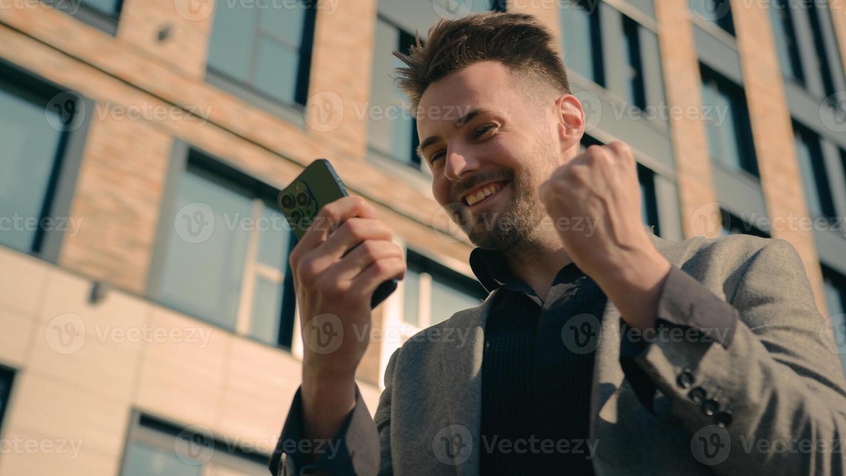 Happy successful caucasian man businessman male guy online winner checking email reading good news using smartphone in city outdoors near office centre enjoying success celebrating victory on phone photo