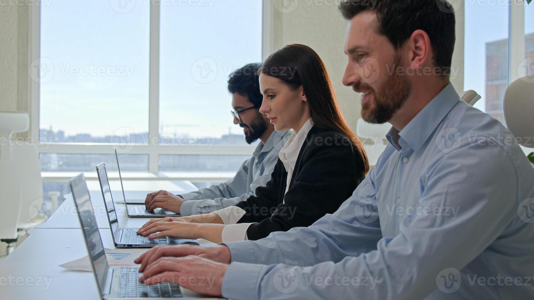 Row of multiracial customer support agents provide service with laptops smiling professional business team programmers businessmen and businesswoman working desktop pc computers at co-working office photo