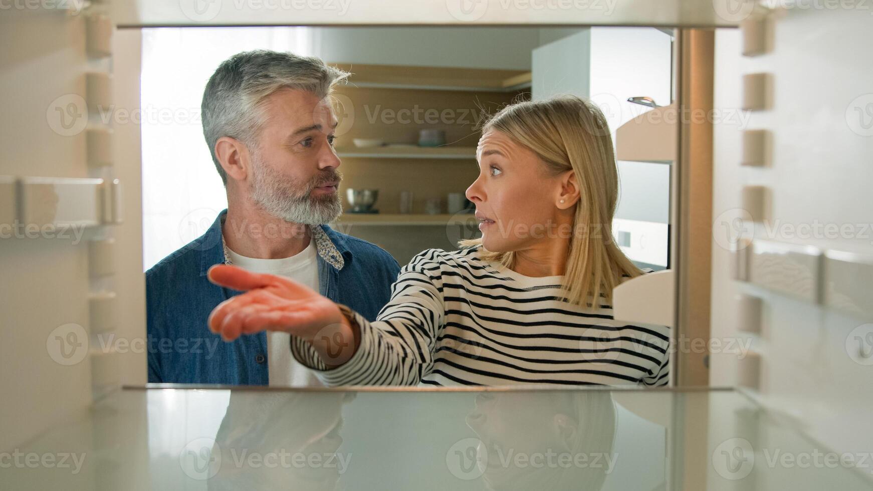 POV point of view from inside refrigerator adults middle-aged Caucasian couple family look at empty fridge nothing to eat need products man find idea problem solution happy smiling order food delivery photo