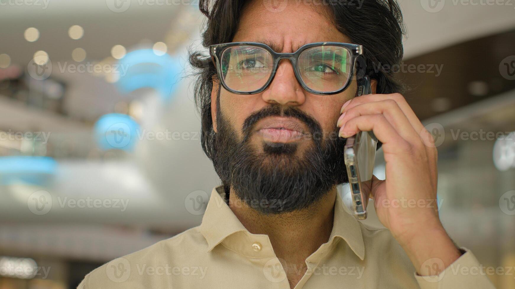 Serious Hispanic Indian businessman executive in glasses Arabian bearded man talking mobile phone smartphone business conversation talk speak call cellphone calling ordering distant negotiate indoors photo