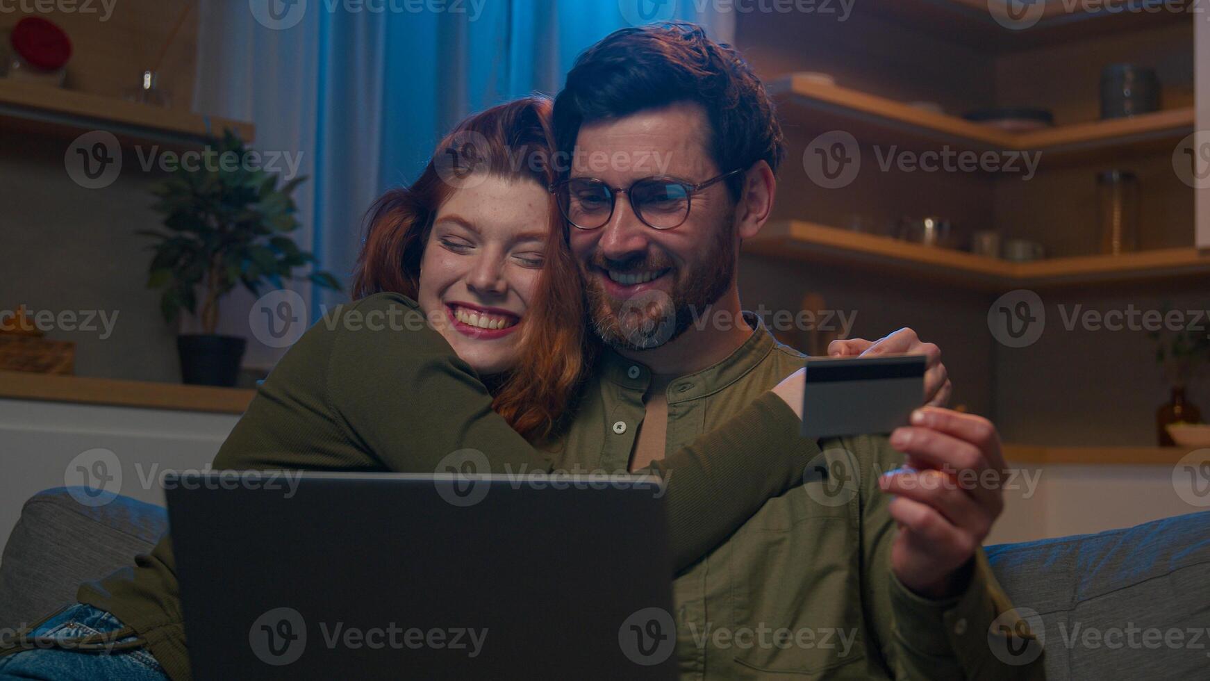 Caucasian male using smartphone on couch home evening loving wife hugging husband smiling man and woman customers shopping in online store on cellphone looking phone screen happy family married couple photo