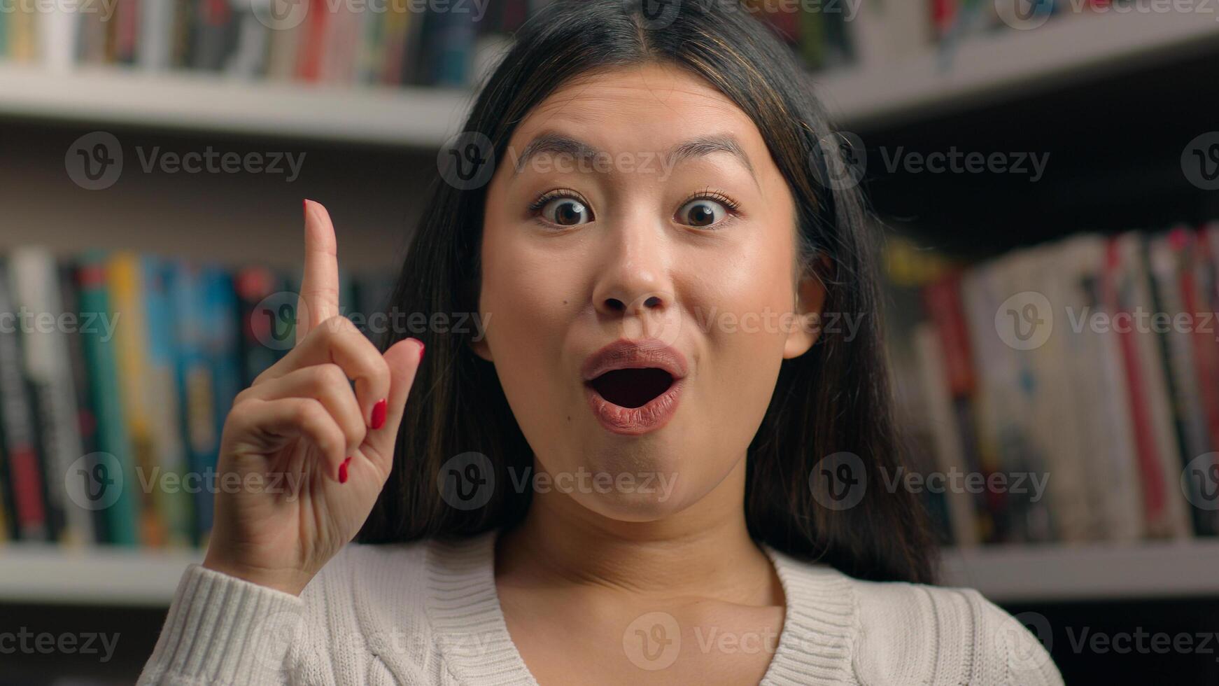 Female portrait smiling happy asian woman girl student 20s looking at camera in university library showing thumbs up like gesture approval symbol successful feedback recommendation agree great result photo