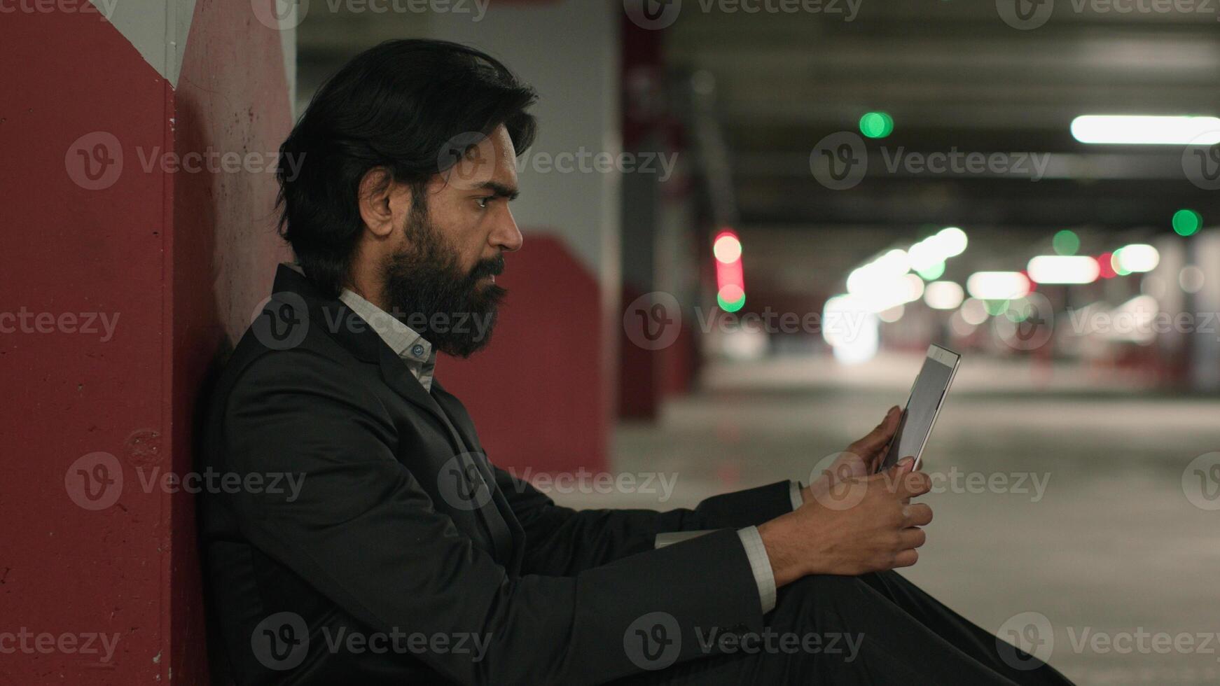 Worried stressed indian man using laptop in underground parking reading bad news on social media frustrated sad jobless arabian businessman looking for job on internet experiencing financial problems photo