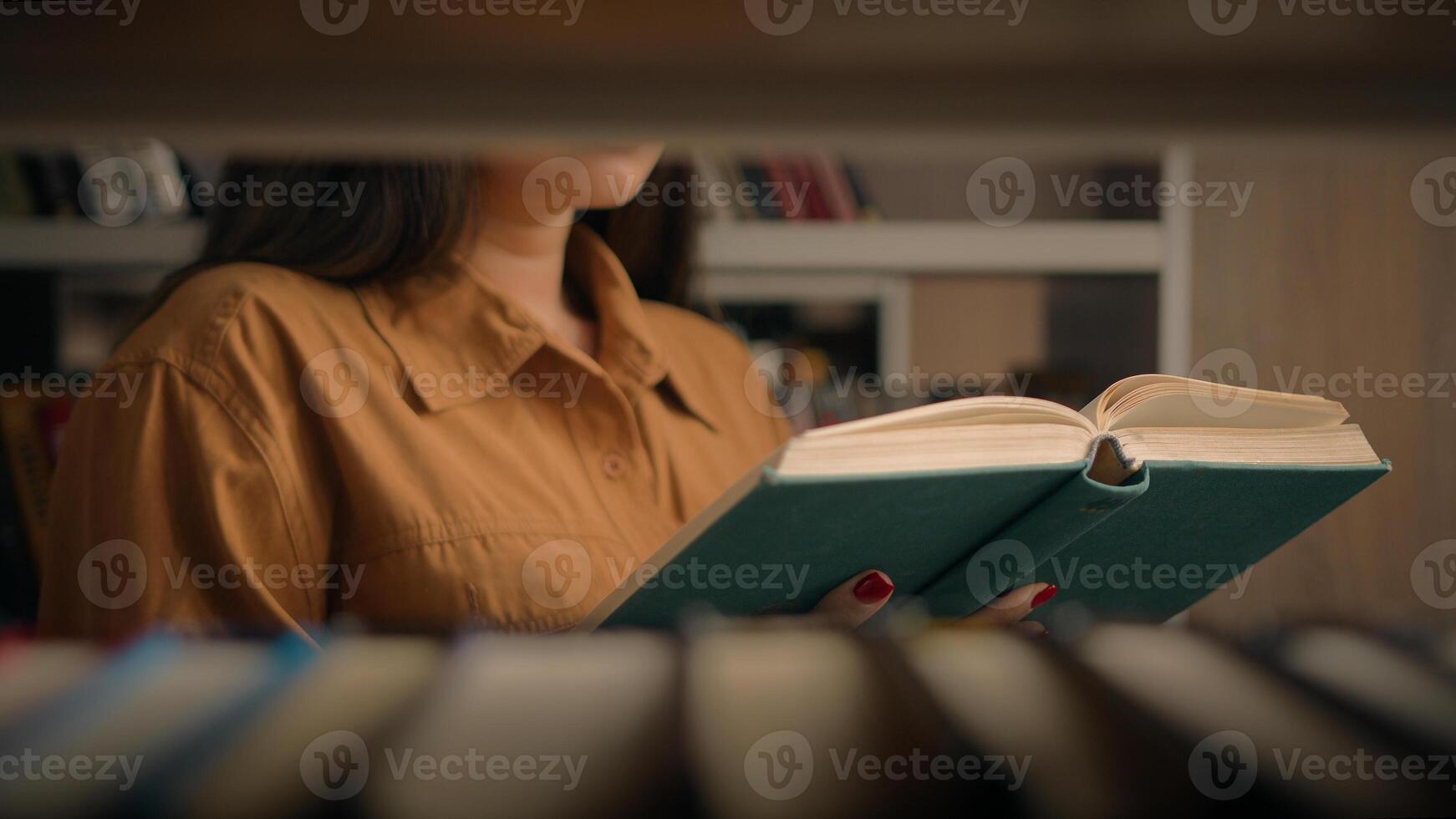 Unrecognizable woman reading book in university library near bookcase smart female girl college student teacher read textbook literature prepare for exam studying homework view through bookshelf books photo