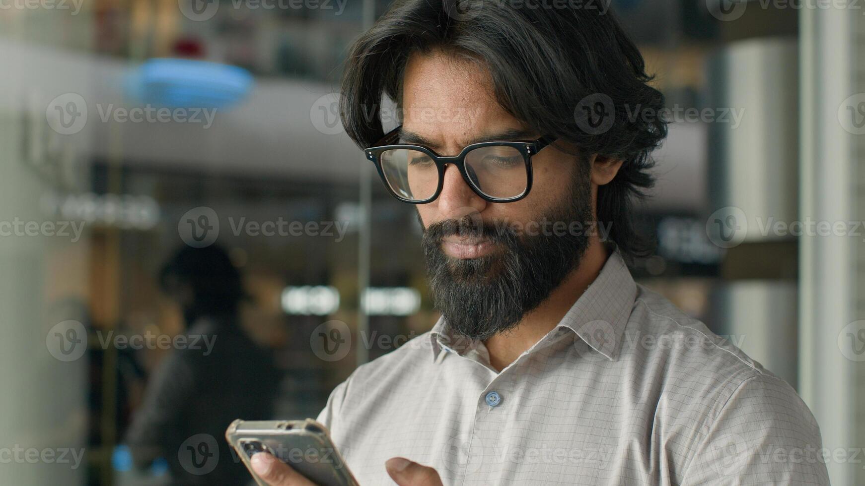 Happy young indian businessman holding smartphone sending message sitting indoors smiling arabian man play mobile game using application on phone reading good news on internet chatting in social media photo