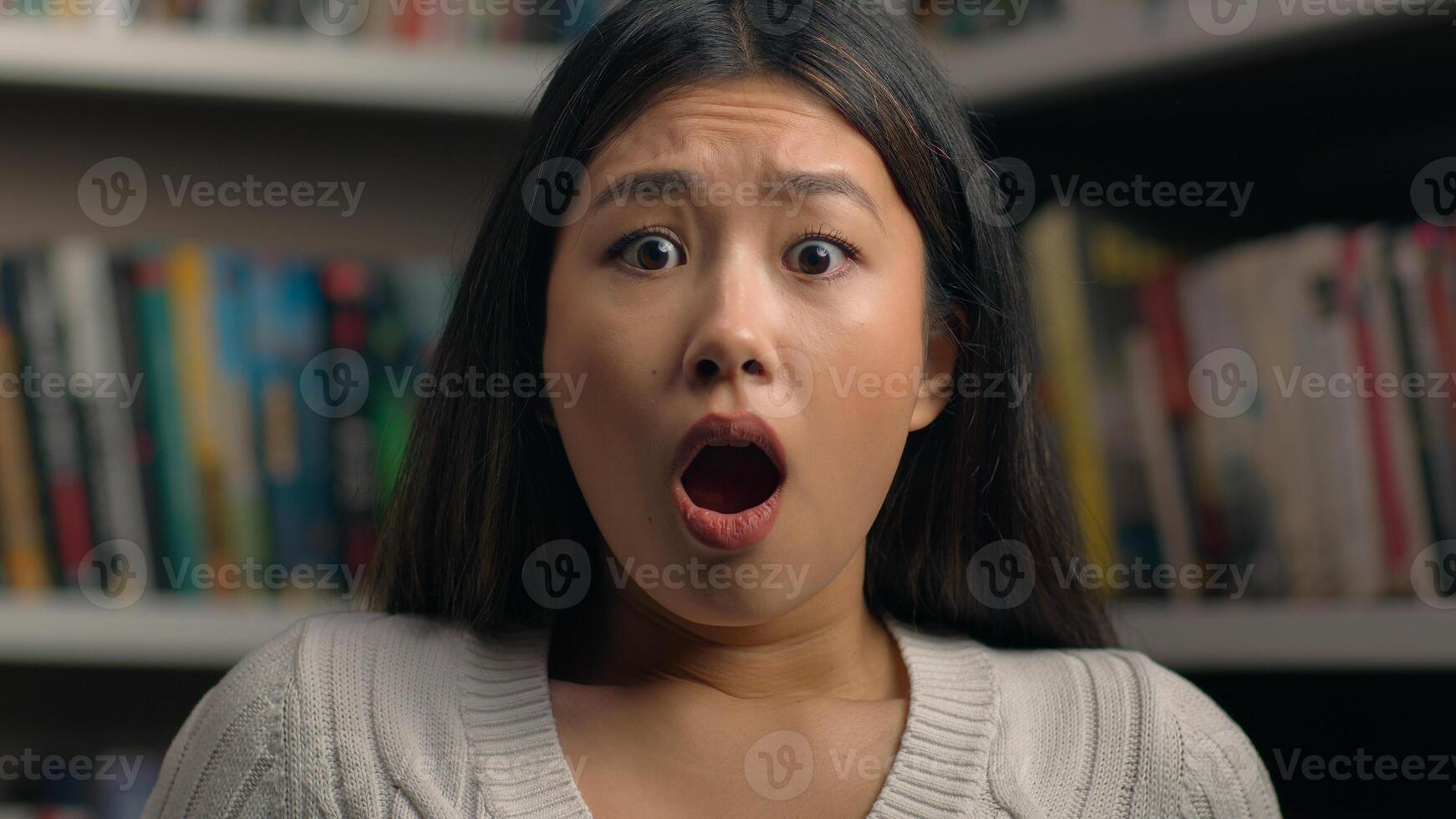 Close-up surprised young asian woman in shock with frightened expression opens mouth shocked by bad news feeling stress female student teacher standing in library near bookshelf worries about problem photo