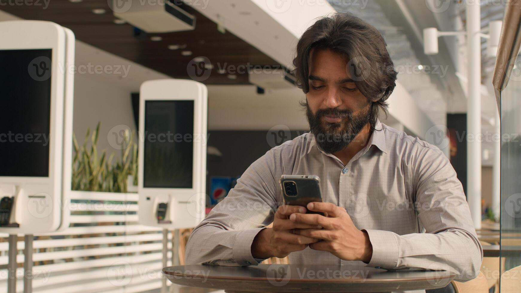 Happy young indian businessman holding smartphone sending message sitting indoors smiling arabian man play mobile game using application on phone reading good news on internet chatting in social media photo