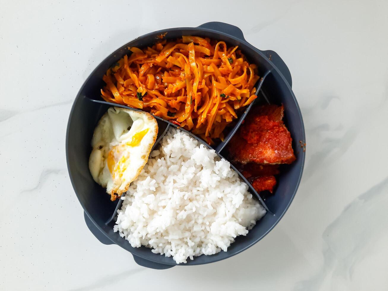 Traditional Indonesian Lunch Box with Rice, Fried Egg, Vegetables, and Fried Fish photo