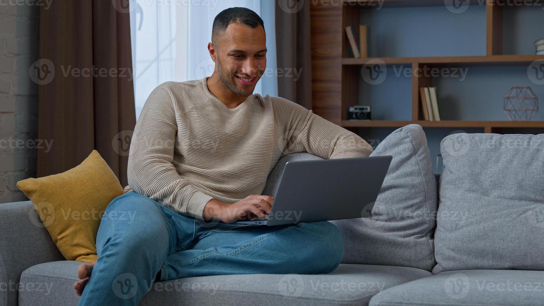 Millennial 30s african american adult man ethnic businessman freelancer sit on couch use pc laptop typing on keyboard distant working chatting online read e-mail e-commerce use home wi-fi networking photo
