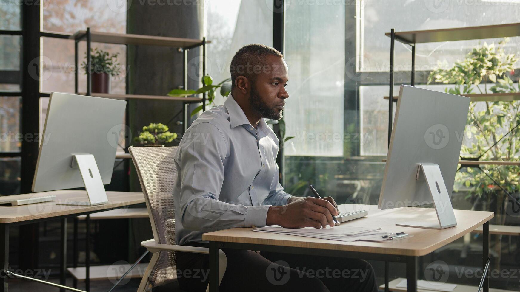 African american mature senior businessman 50s ethnic man sit in sun shining sunlight office banker manager write notes business documents writing text on paper count loan bills enter data at computer photo