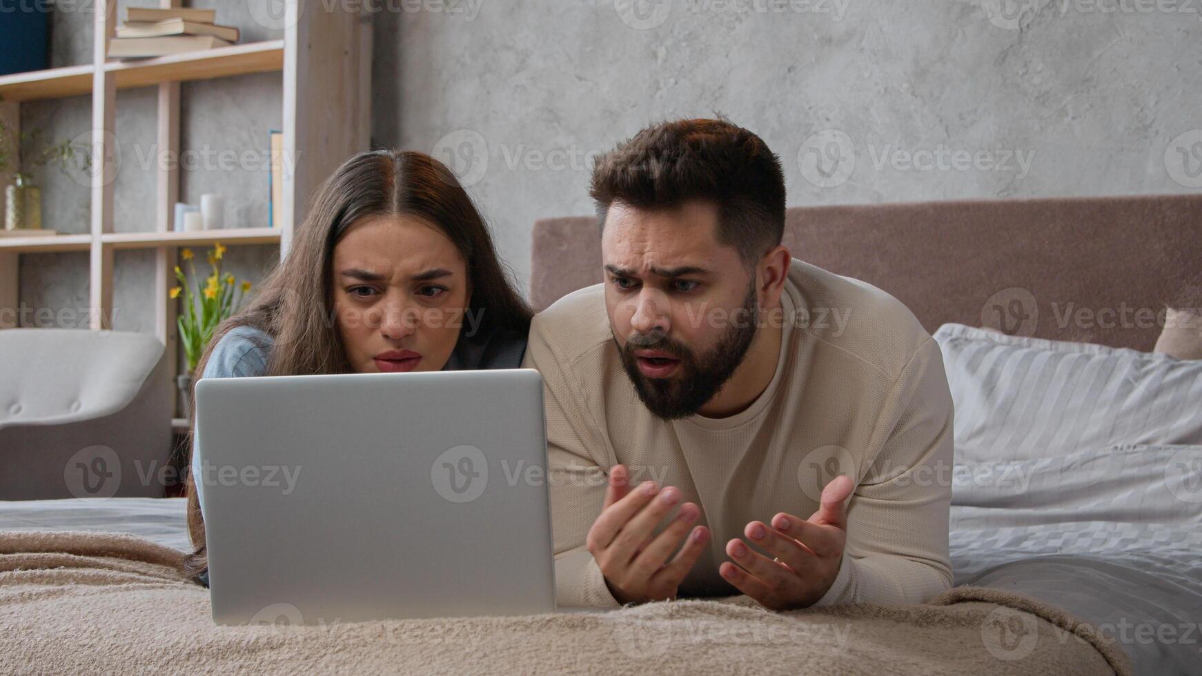 Desperate stressful Caucasian sad couple homeowners confused family wife husband read bad email trouble lost bank mortgage negative result computer failure anxious man and woman lying on bed at home photo