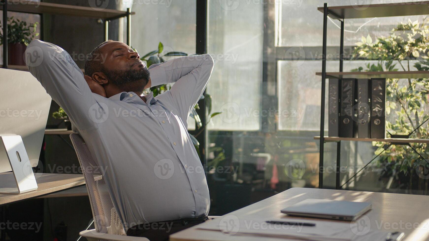 Relaxed African American mature businessman senior happy man finish computer work close laptop relaxing in sunny warm comfortable office male specialist stretch muscles put hands behind head day end photo