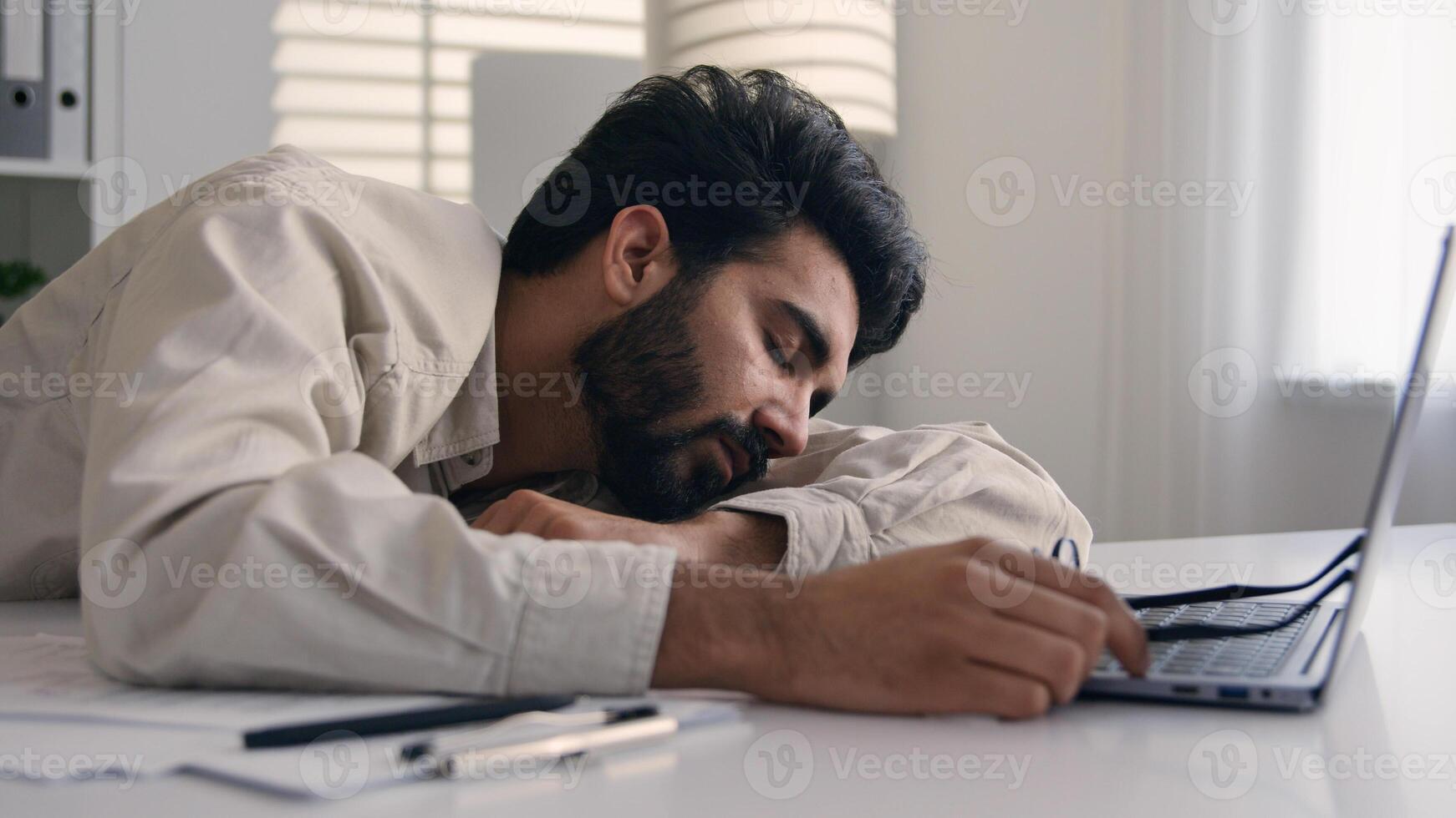 Lazy weary sleepy male manager tired exhausted Arabian Indian businessman employee working computer boring remote job man fall sleep on desktop napping in office overwork fatigue no energy sleeping photo