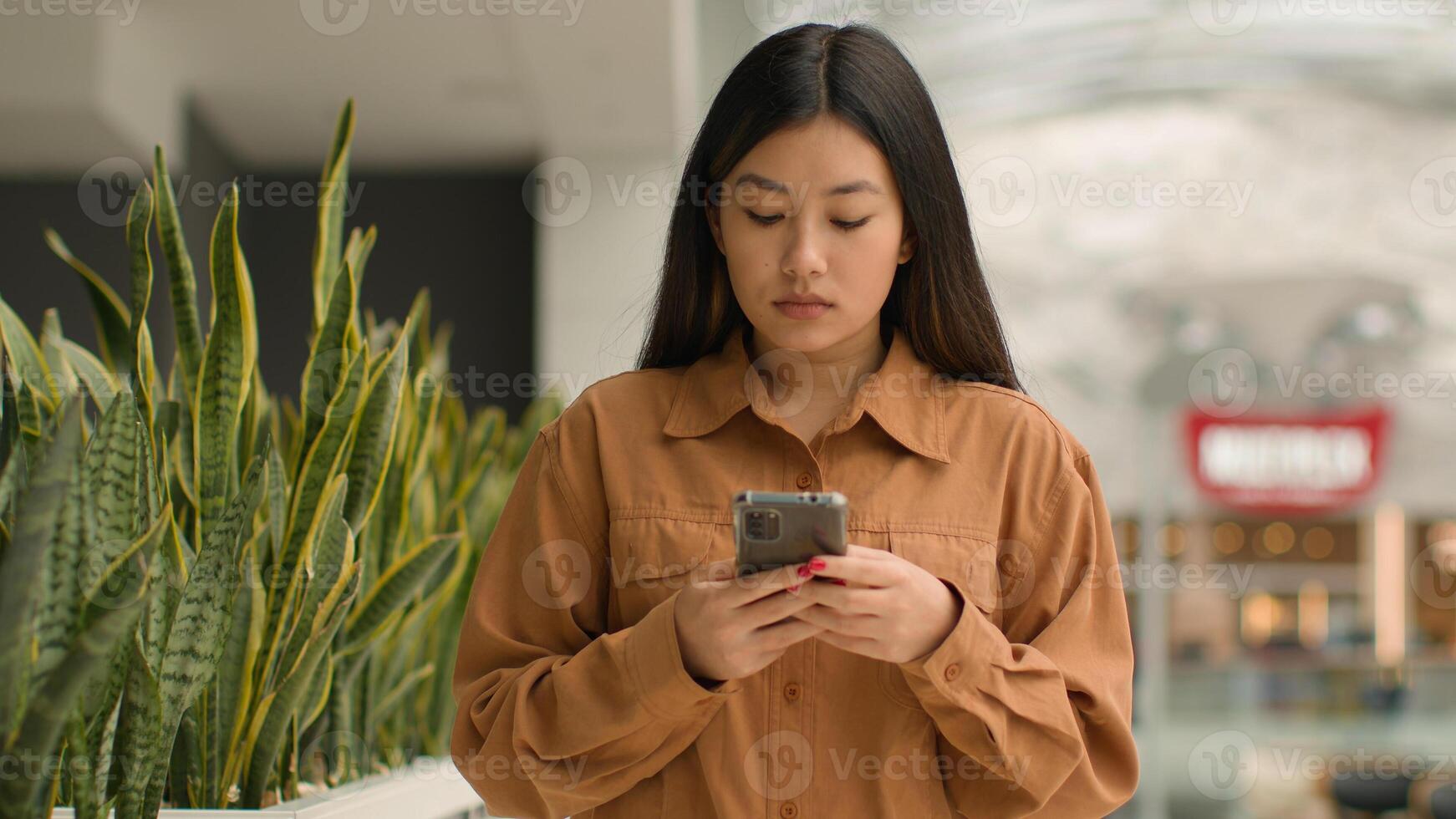Asian focused woman walking in shopping mall with smartphone look at mobile phone screen Chinese korean girl businesswoman customer walk chatting message online use cellphone app buy in internet store photo
