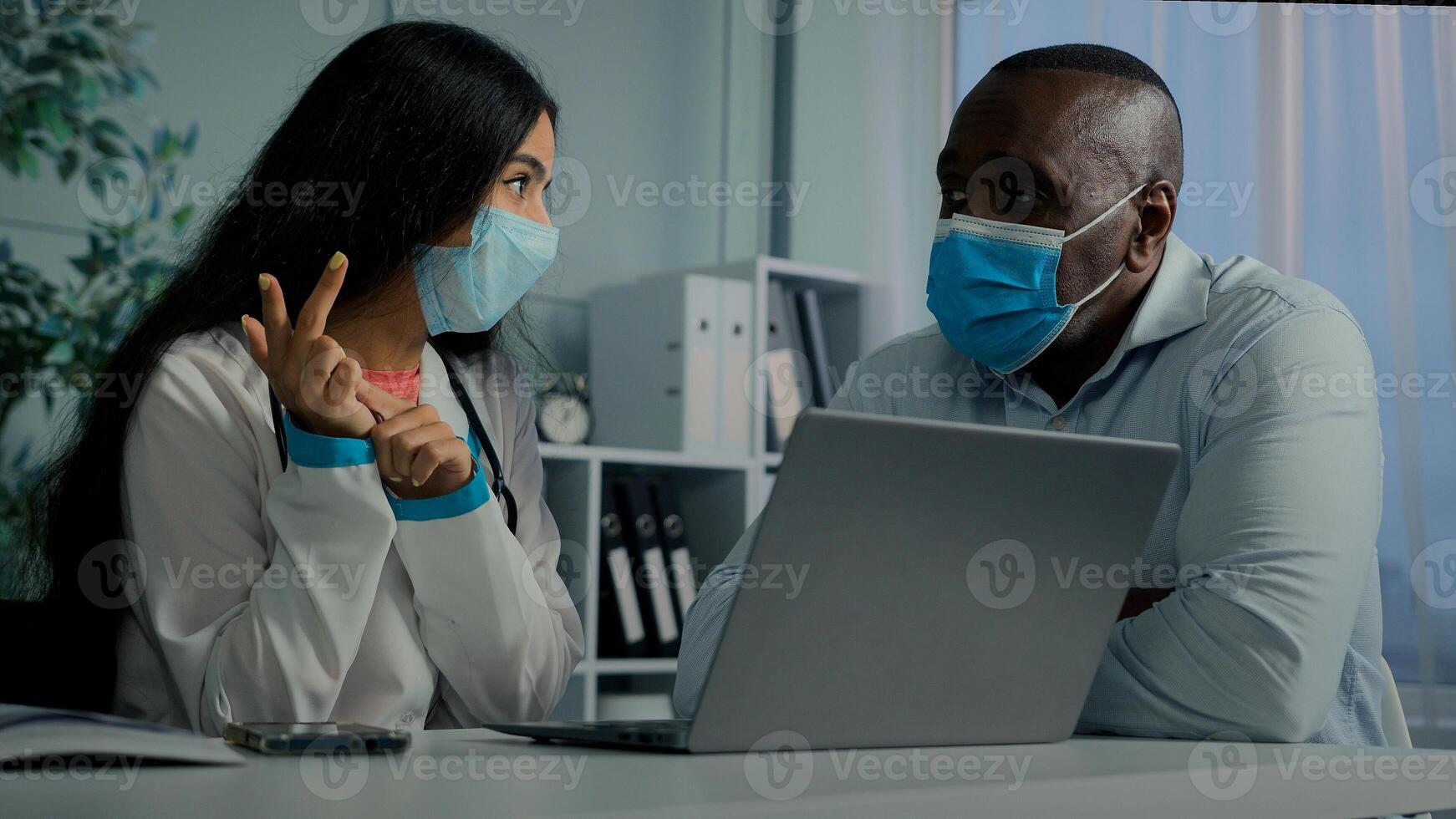 Young doctor woman talk with old man patient in mask use laptop check electronic health test result service online medicine register elderly client on computer modern tech give medical recomendation photo