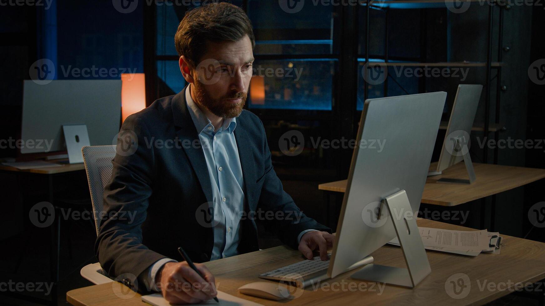 Middle-aged worker adult 40s Caucasian man teacher male executive manage business tasks write notes paper invoice signing document insurance writing paperwork in evening office search data on computer photo