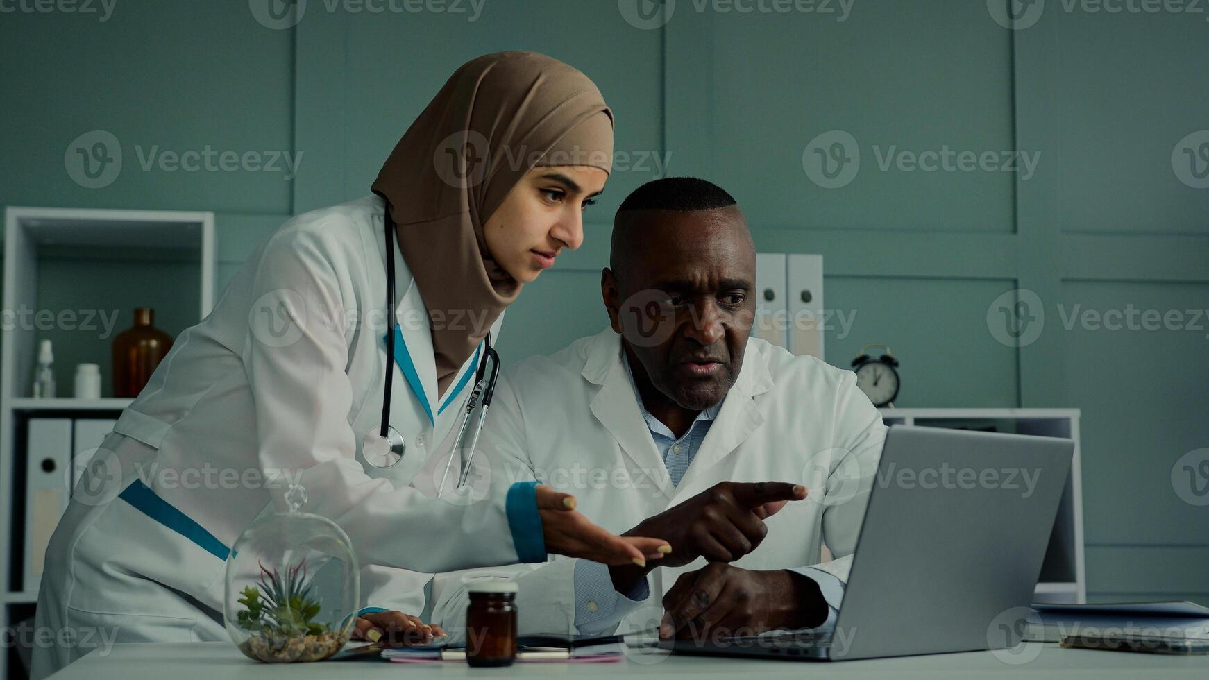 Multiracial doctors colleagues discuss teamwork african man and arabian woman two professional medical workers talk about healthcare check MRI scan use computer app doing online research X-ray results photo