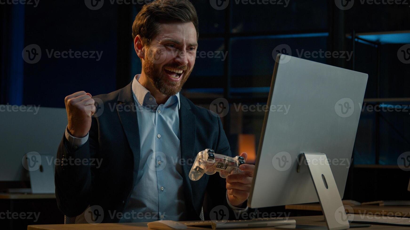 Adult businessman employee working in evening office happy male gamer Caucasian man take break playing console game on computer with gaming controller using joystick gamepad play virtual match photo