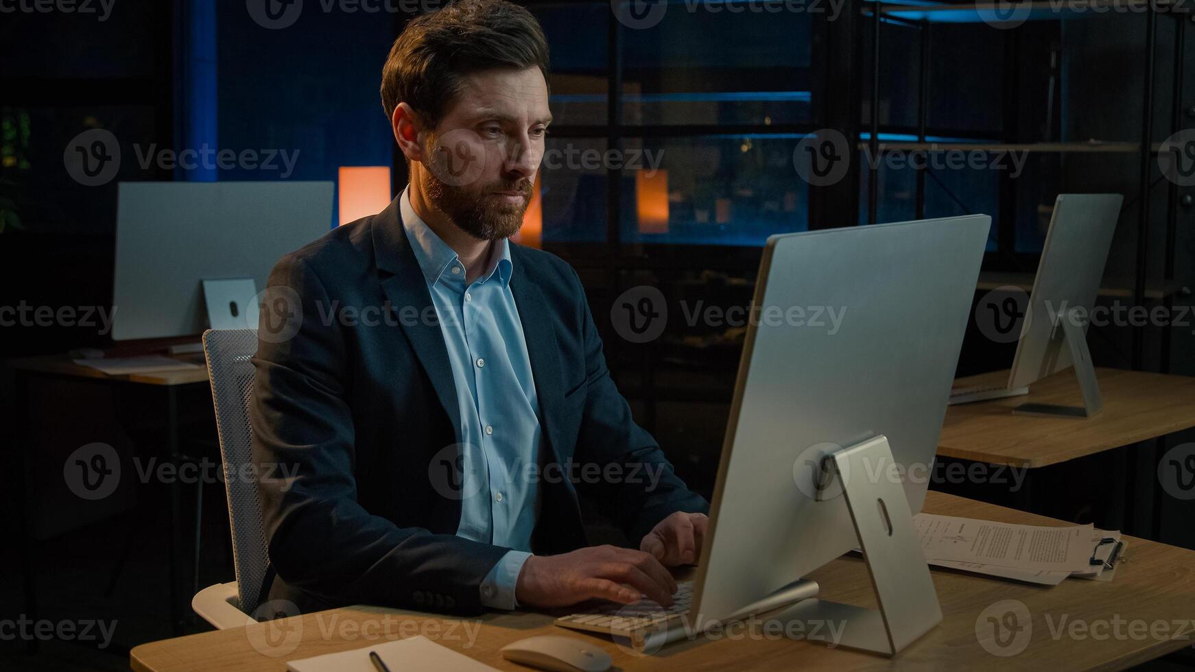 Male business portrait confident focused businessman millennial caucasian senior 40s adult man chief boss leader sit at desk with computer search online data working alone in evening office indoors photo