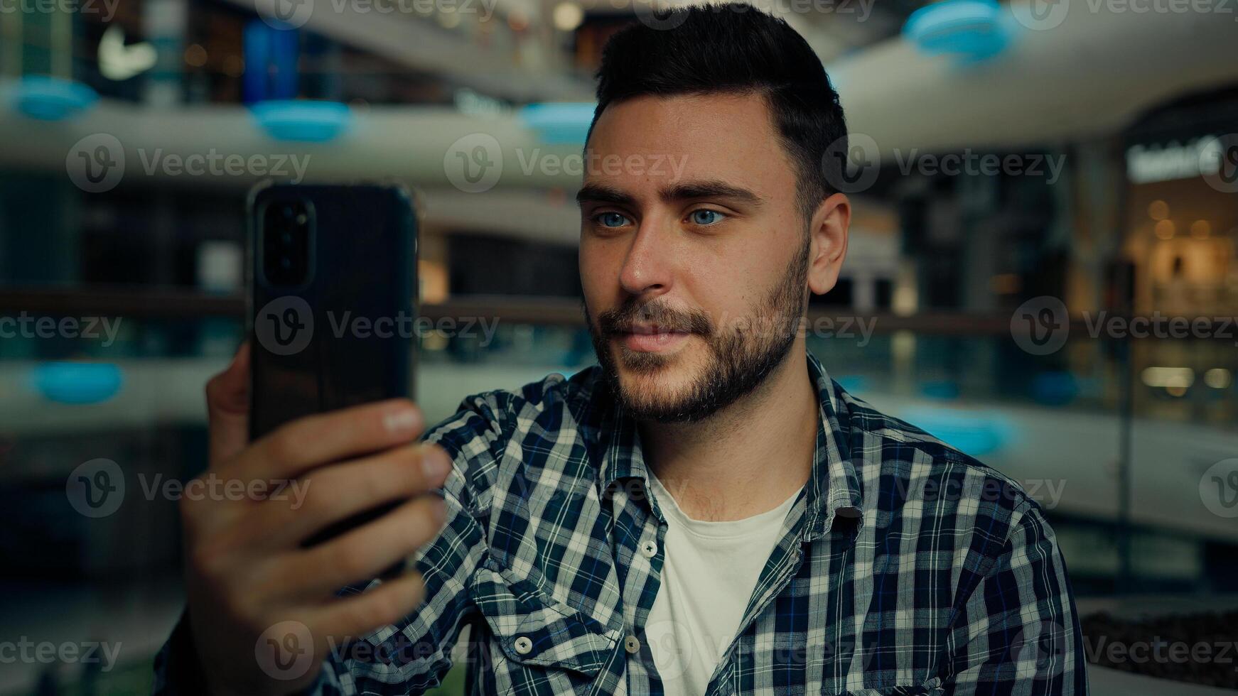 Smiling arabian caucasian male blogger businessman look at mobile phone camera talk call in shopping mall happy young man chatting online recording blog use modern tech for remote communication photo