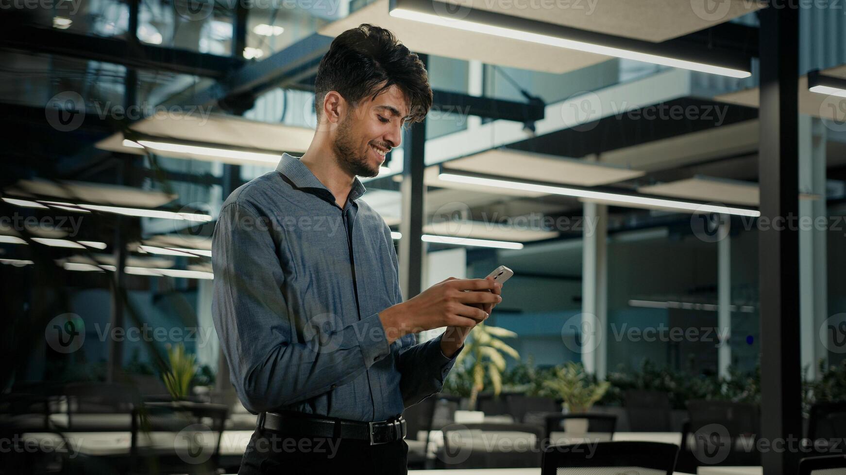 Smiling happy millennial arabian businessman ethnic man professional office worker male guy use smartphone browsing mobile apps look at cellphone texting message chatting online make order in internet photo