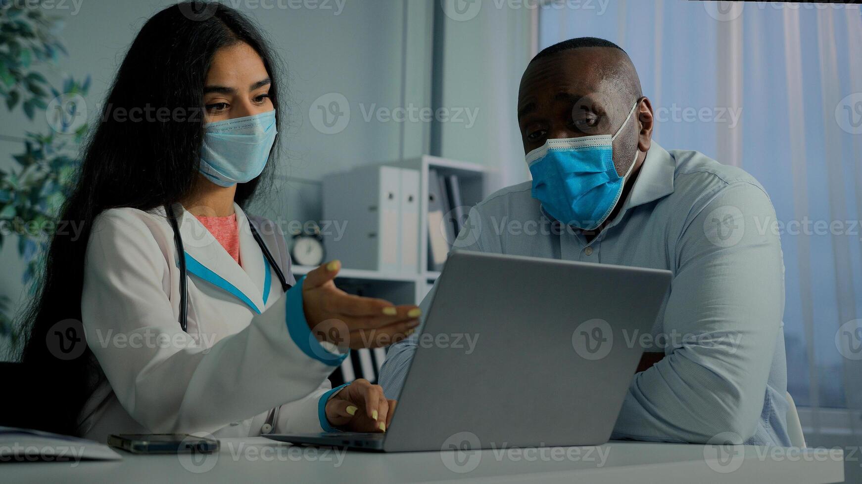 Young doctor woman talk with old man patient in mask use laptop check electronic health test result service online medicine register elderly client on computer modern tech give medical recomendation photo