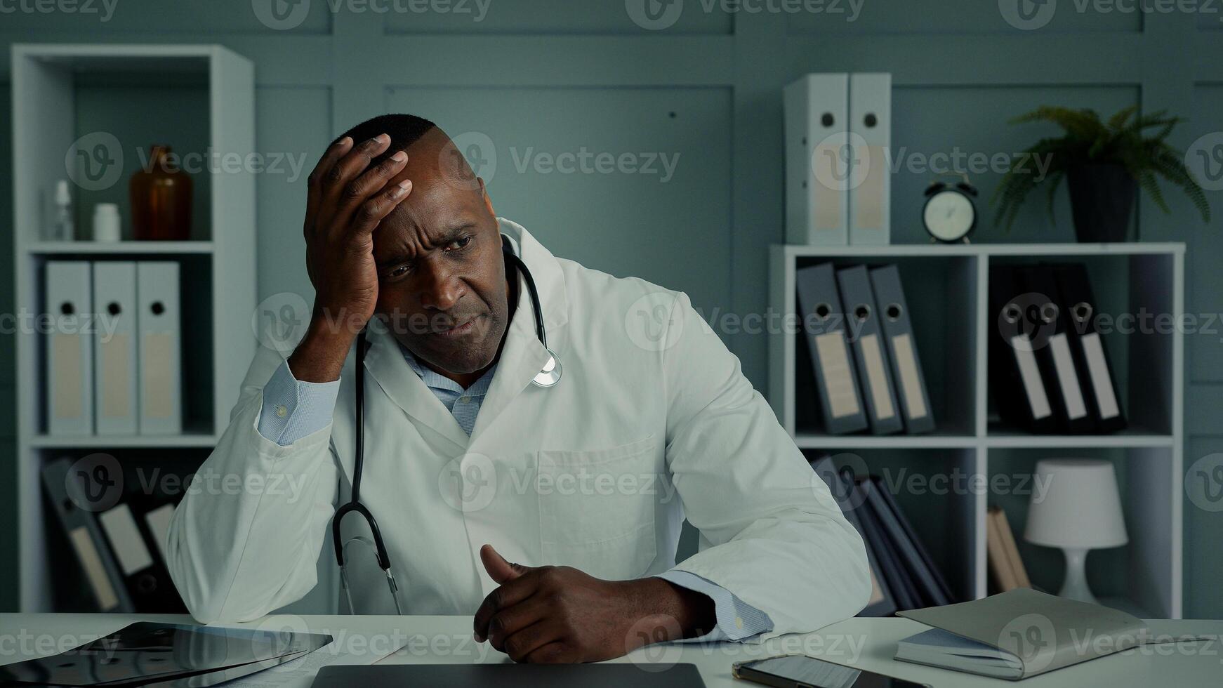 Pensive thoughtful sad african doctor ethnic elderly age man feel despair stress exhausted tired male sit at hospital think health problem depress syndrome professional burnout sorrowful face emotion photo