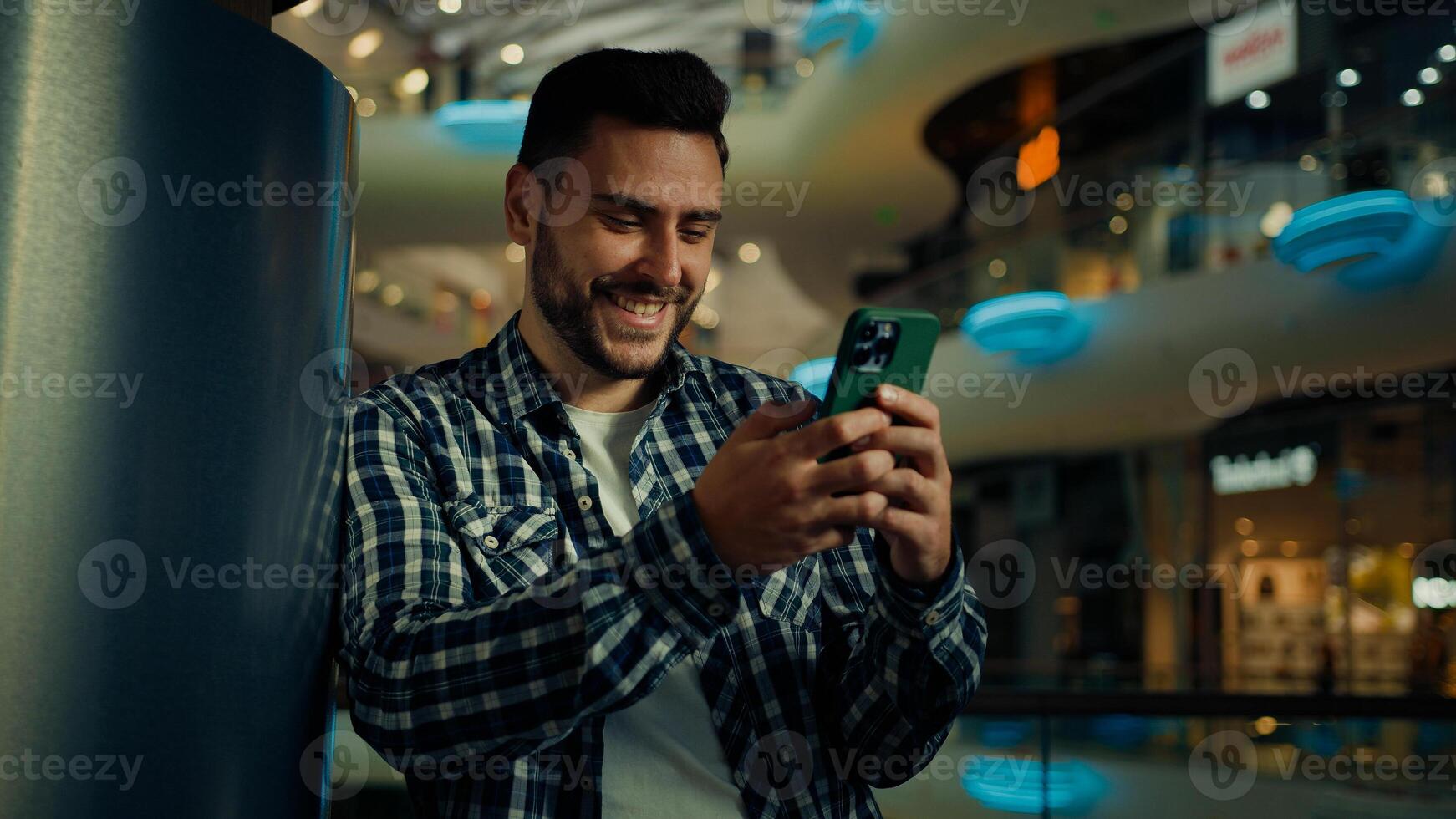 Young man blogger arabian hispanic businessman stand in shopping center look at mobile screen texting message email read positive news on cellphone buying goods online use wireless internet connection photo