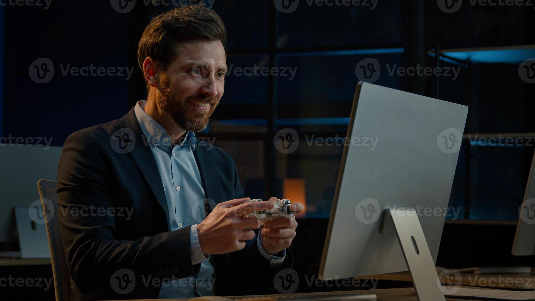 Adult businessman employee working in evening office happy male gamer Caucasian man take break playing console game on computer with gaming controller using joystick gamepad play virtual match photo
