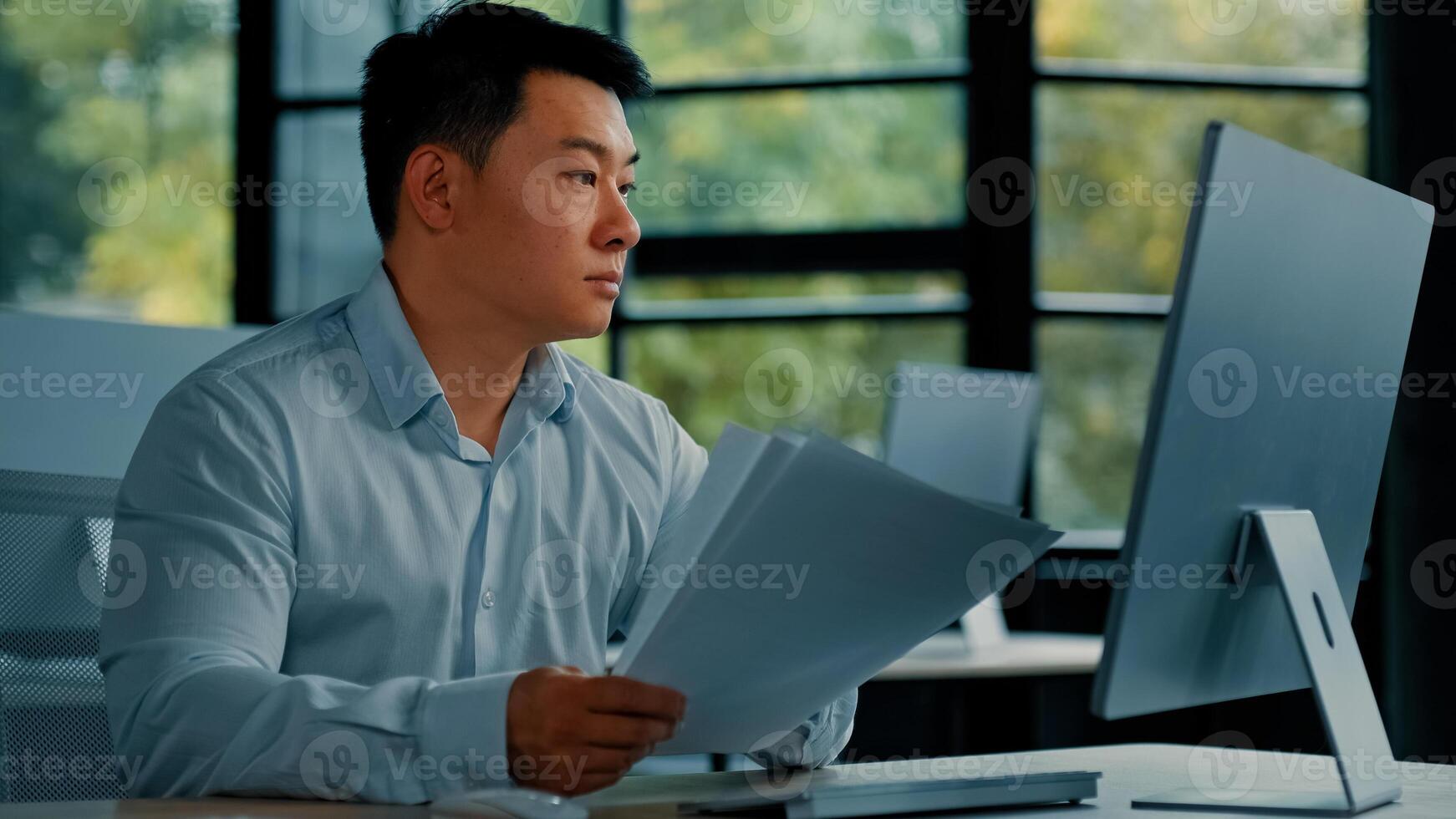 Professional asian businessman korean japanese 40s man lawyer office worker reading financial documents invoice contract budget documentation searching business data at computer paying bills online photo