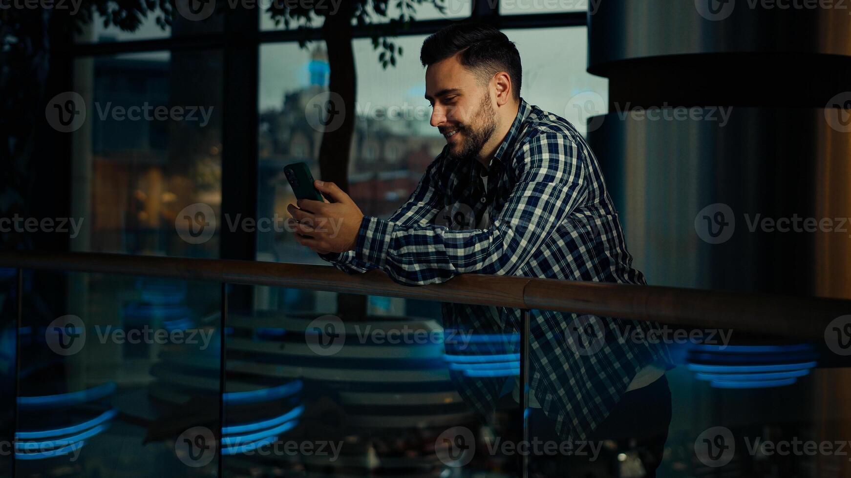 Young man businessman caucasian hispanic male client guy stand in modern business office hold smartphone chatting online use mobile phone banking app browsing website play internet games on cellphone photo