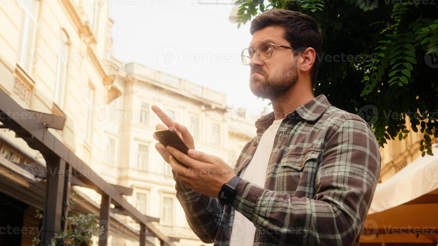 Caucasian man male tourist traveler confused guy walking street outdoors using mobile phone navigator going lost city smartphone gps map online app destination searching address location travel guide photo