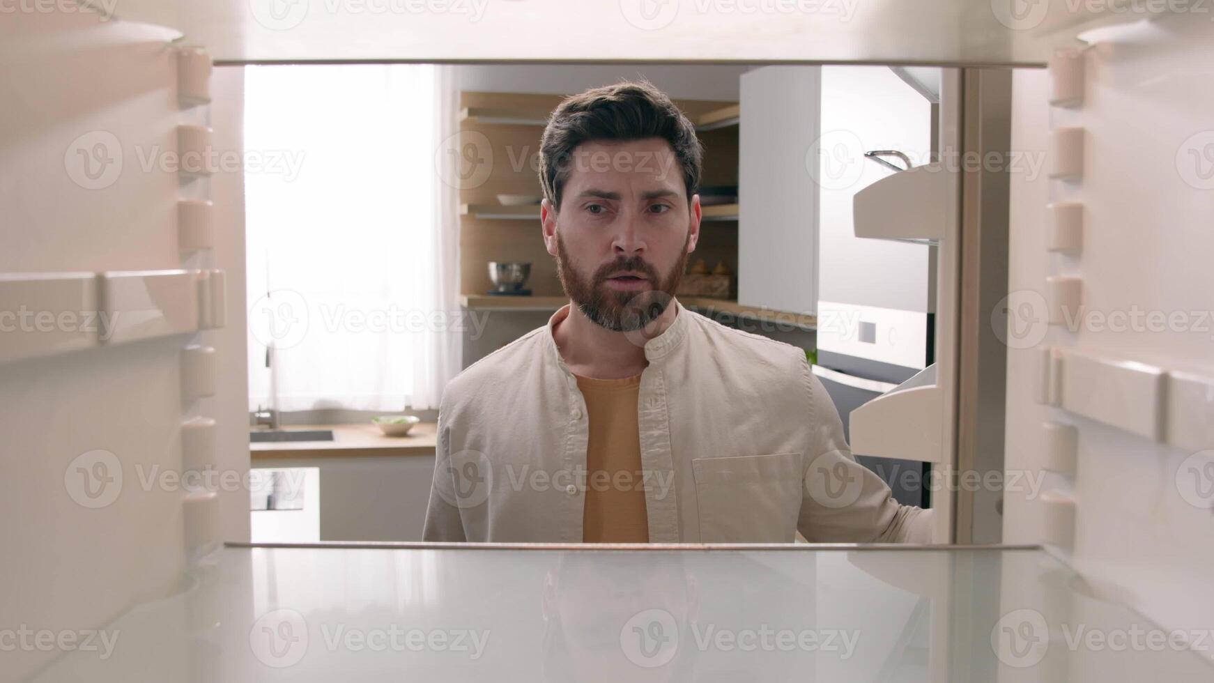 Hungry Caucasian bachelor man looking for food in empty fridge finding no meal products feeling sad disappointed poor unemployment need delivery service POV point of view from inside refrigerator photo