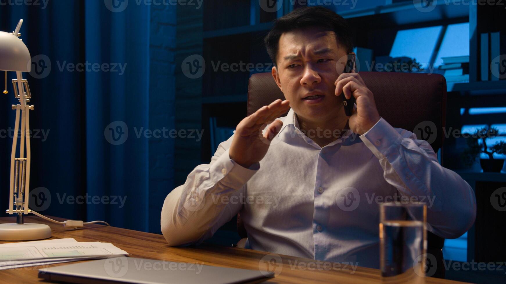 Angry disappointed business employer Asian businessman mad dissatisfied Chinese man stressed Korean entrepreneur argue conflict quarrel misunderstanding talking mobile phone at night evening office photo