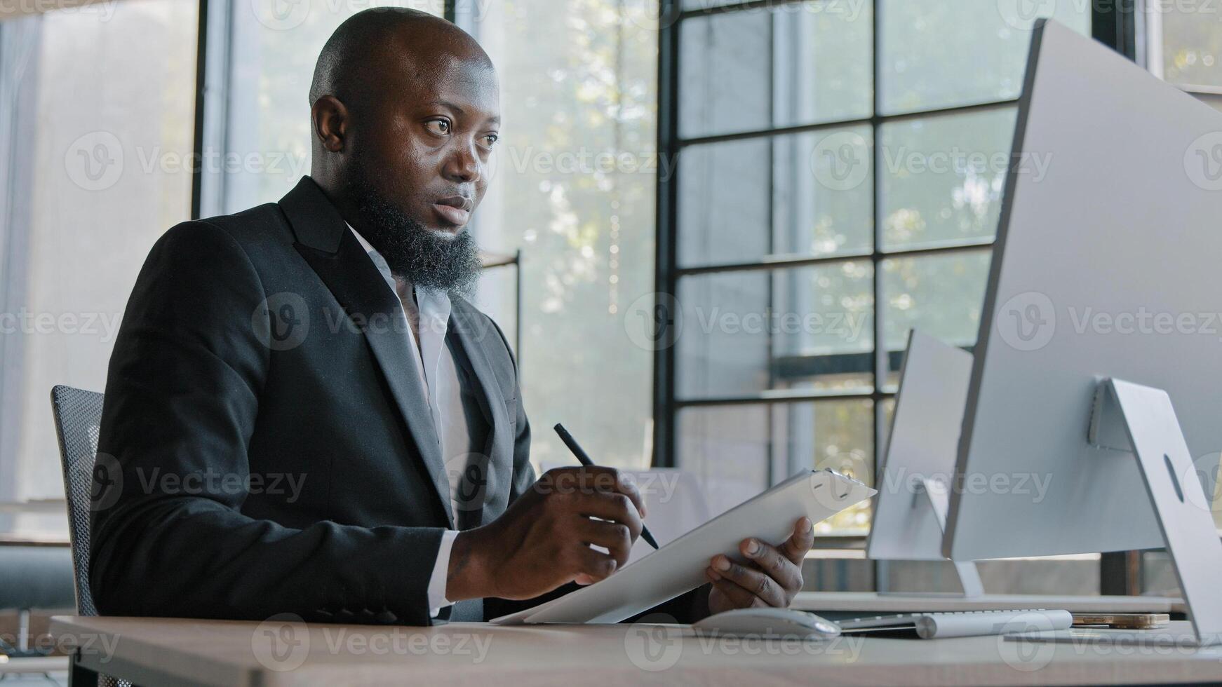 Senior businessman african american right-handed employee designer sit in office look at computer screen writing new information use paper tablet personal planner write business ideas strategy plan photo