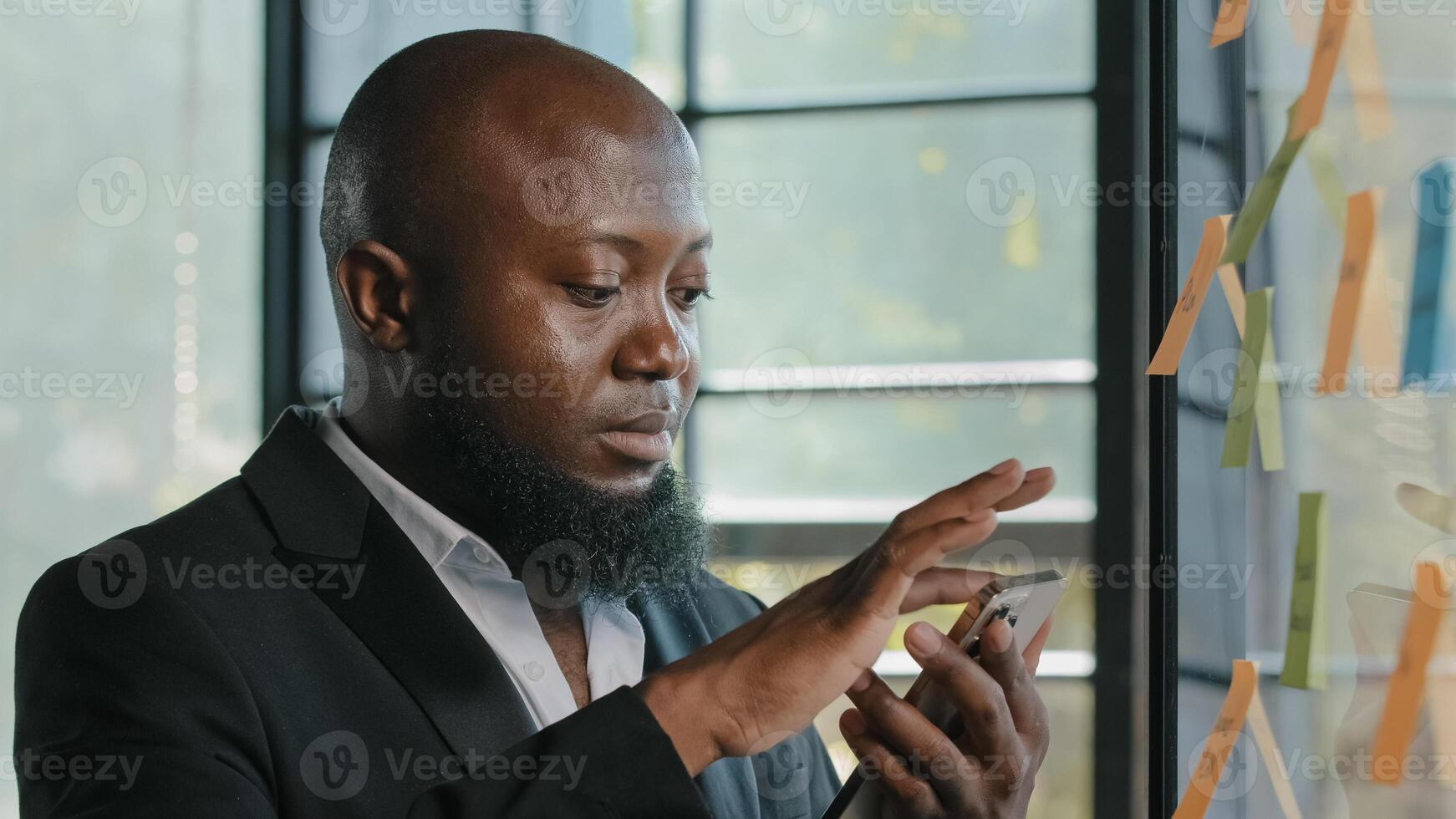 African american businessman stand near sticker board read news on smartphone make online order booking delivery at office use business mobile apps scrolling sensor display chatting in social networks photo