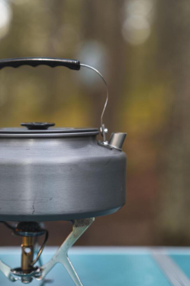 A kettle is heating up on a small camping stove as steam begins to rise in the cool forest air photo