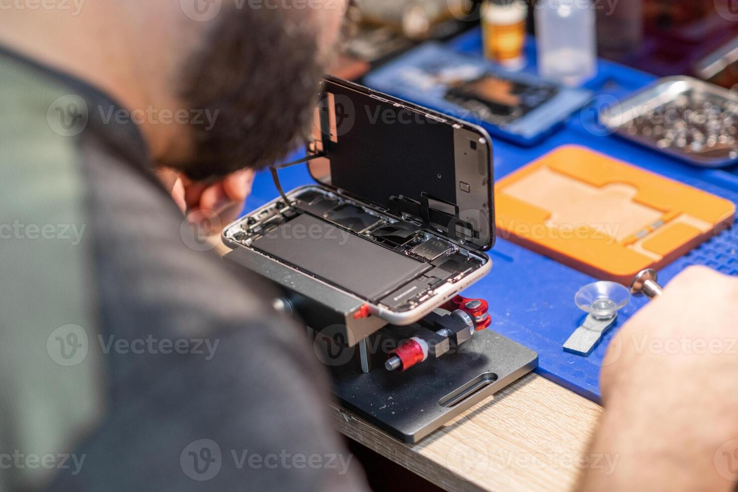 A technician carefully repairs a phone, focusing on battery replacement and intricate components in a busy workshop setting photo