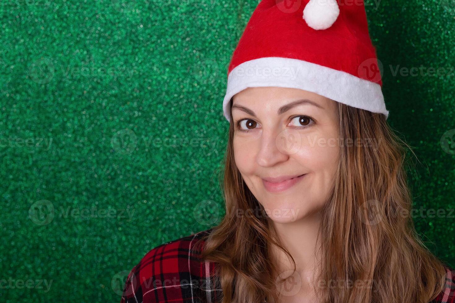 beautiful girl in a shirt on a green background in a New Year's cap smiling. Christmas. New Year photo
