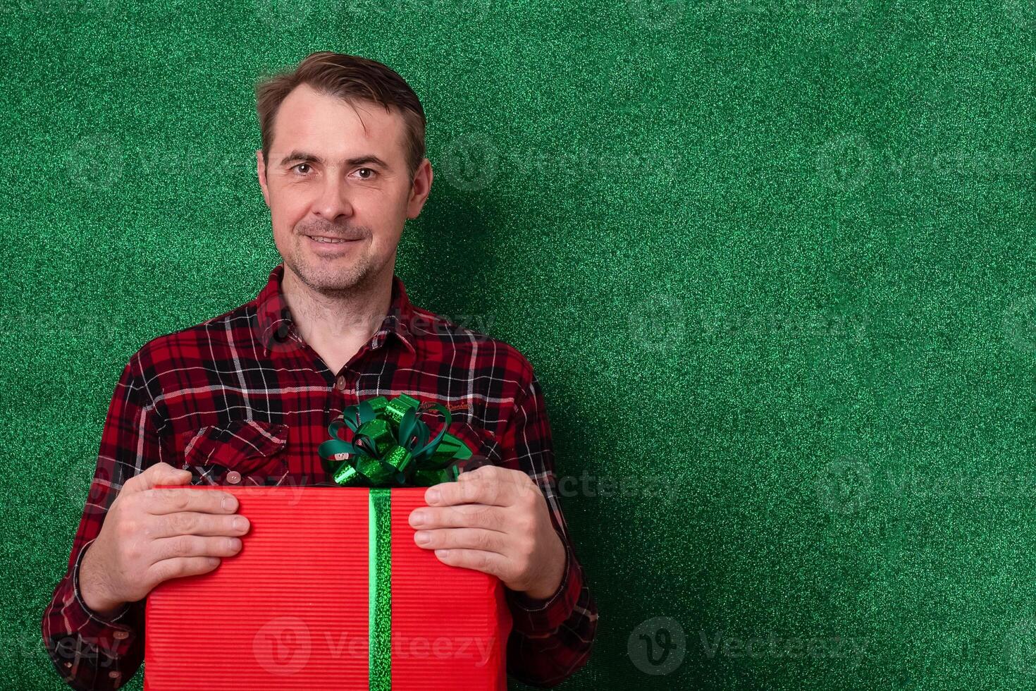 a man with a gift in his hands on a green background looks into the frame. holidays new year, valentine's day photo
